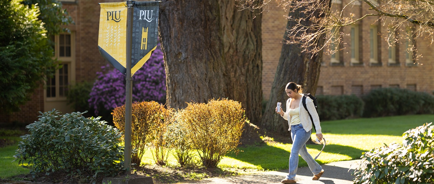Web Banner - Student Walking on Campus Female student walking on university campus path near PLU banner