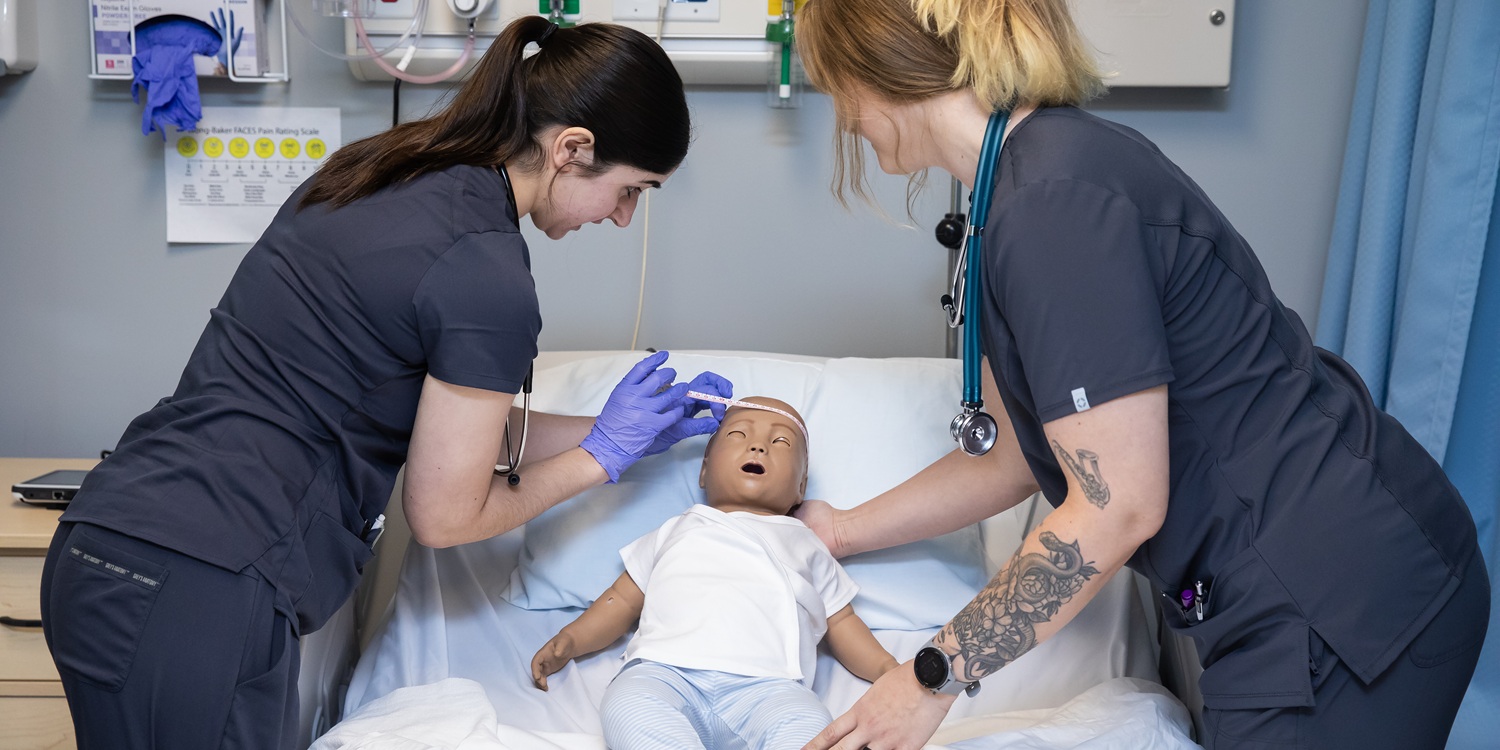 Web Banner - Nursing 02 Two nursing students practice in PLU's simulation lab on a simulation baby patient.