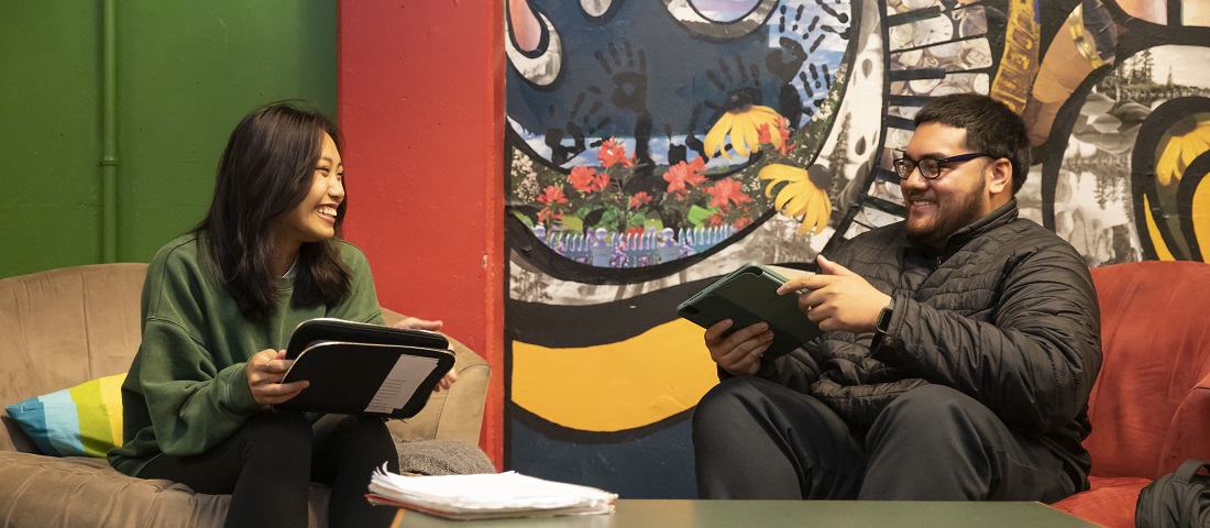 Two students smile at each other while studying together in PLU's CAVE, a student commuter space