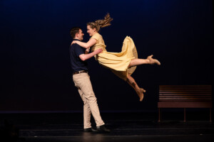 A woman in a yellow dress is swung around by a male partner with her ponytail streaming behind her.