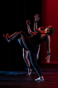 Students wearing black and with arms and legs akimbo are lit in red and blue light.