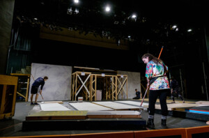 Set prep and construction as two students paint set panels laying on the floor.