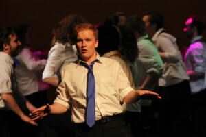 A man in a white shirt and blue tie sings.