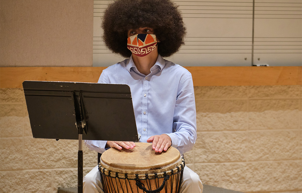 A student wearing a mask participates in the Percussion Studio rehearsal.