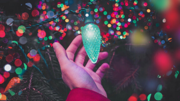 Sparkly Christmas lights and a hand reaches for an oversize green light bulb