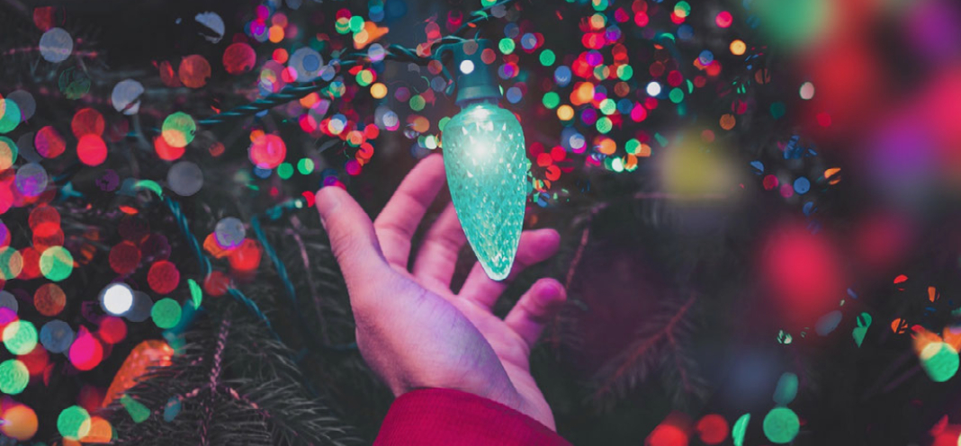 Sparkly Christmas lights and a hand reaches for an oversize green light bulb