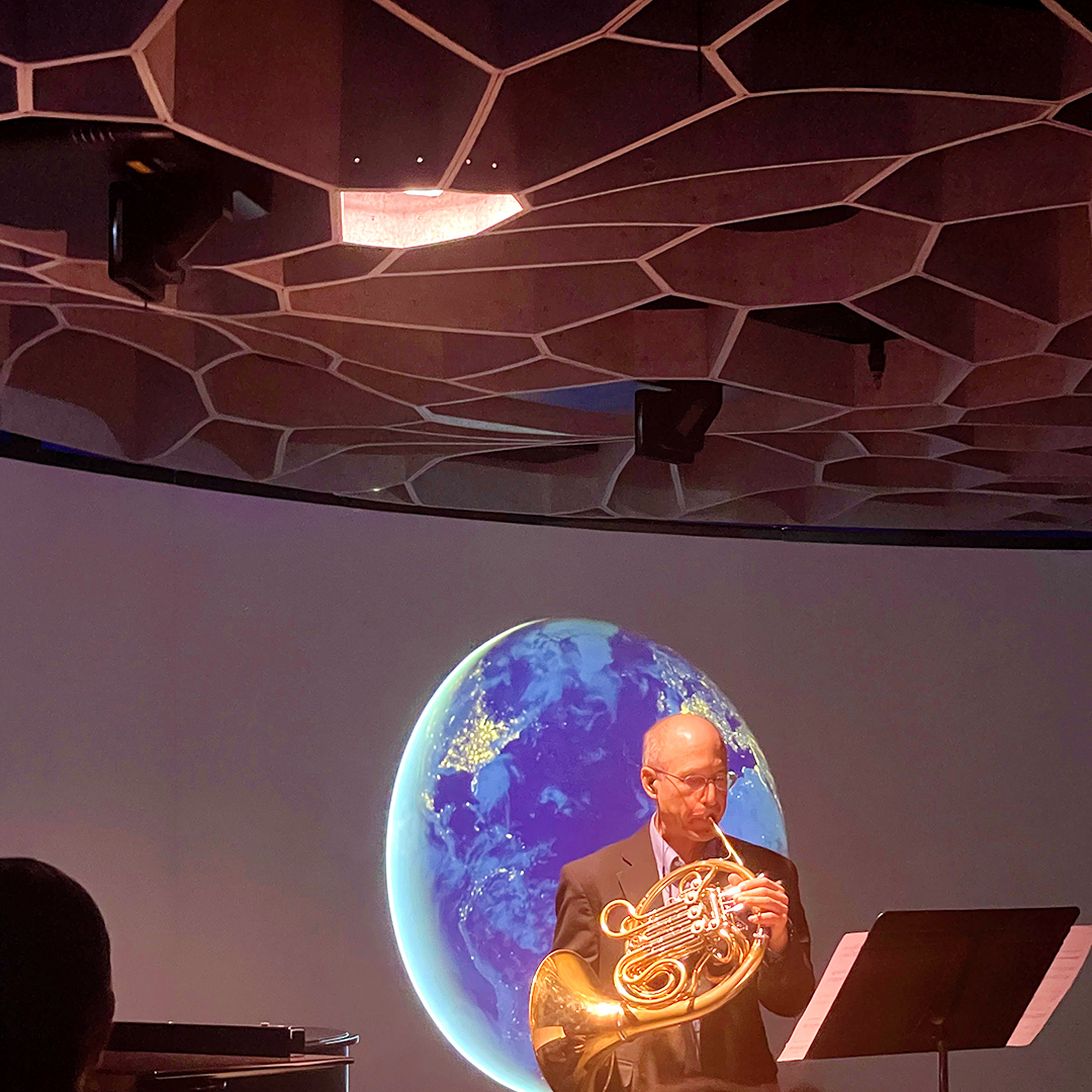 Mark Robbins, Associate Principal Horn of the Seattle Symphony, performing the premiere of Pale Blue Dot in front of an image of the Earth