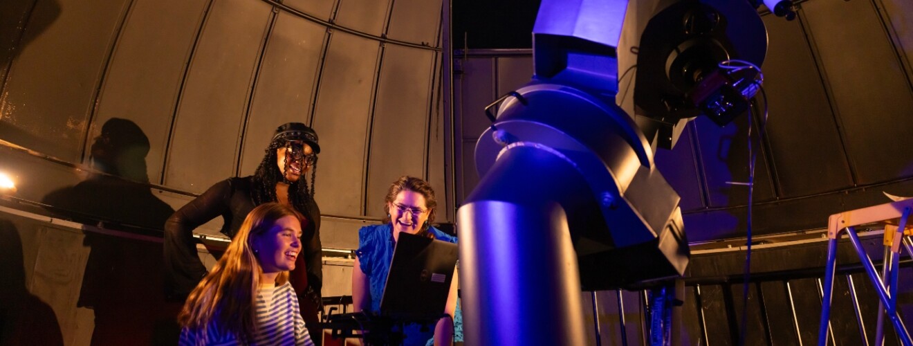 two students and a professor looking into a telescope