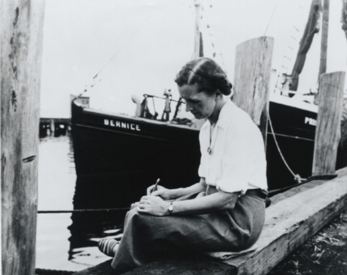 Rachel Carson Writing With a Pencil On a Dock, Seated Beside a Boat Named 'Bernice' - courtesy of the Beinecke Rare Book and Manuscript Library, Yale University