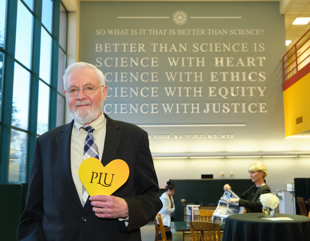 William Foege '57 poses in front of a wall in the Rieke Science Center which features his quote.