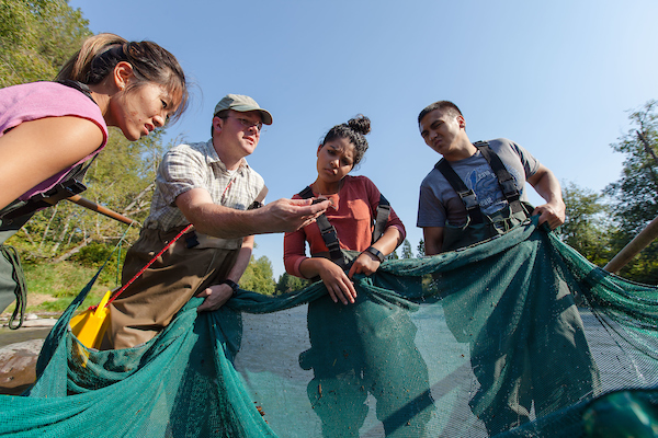Professor Egge with a net in the river surrounded by students