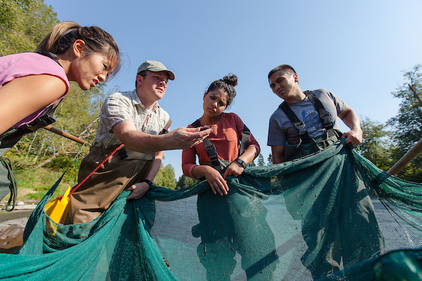 Professor Egge with a net in the river surrounded by students