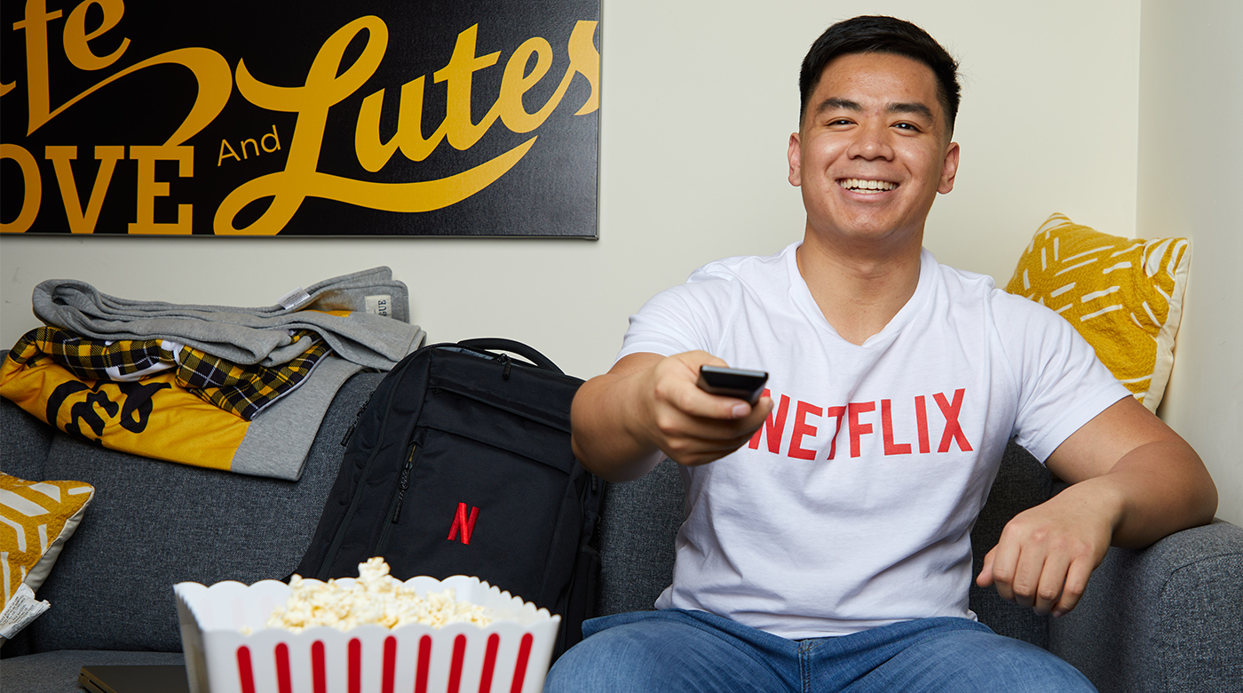 Adrian on the couch with a remote wearing a Netflix shirt