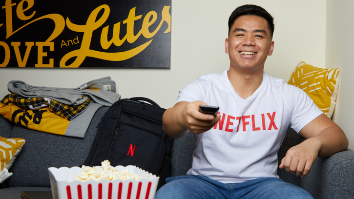 Adrian on the couch with a remote wearing a Netflix shirt