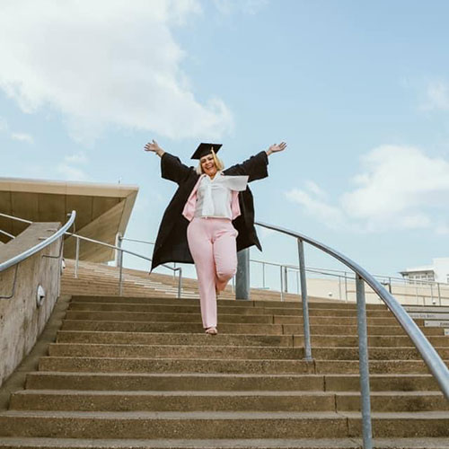 Elizabeth Larios on stairs with graduation hat and gown.