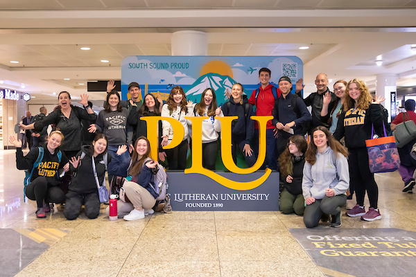 Students gathered around the PLU sign at SeaTac airport.