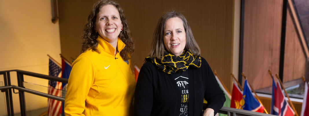 Dr. Ann Auman and Dr. Bridget Yaden pose in front of international flags.