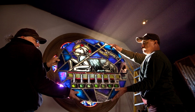 Paul Martinez and Ramon Coronado in a shaft of dusty light while reinstalling the rose window. (Photo by John Froschauer)