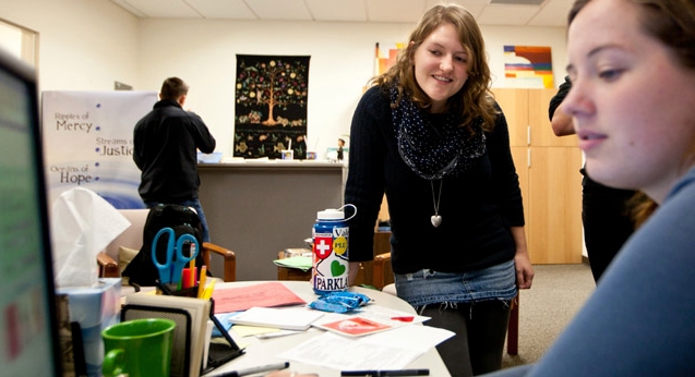 Laura Rudquist ’12 (center) talks with a colleague at Campus Ministry offices during her regular shift. Rudquist, from Minnesota, said PLU feels like home, yet still challenges her in her studies and world view. (Photo by John Froschauer)