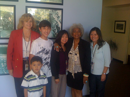 Sheryl Wold ’76, far left, poses with Nichelle Nichols – who played Lt. Ohura in Star Trek — after a ride on the Advance Cab 747 simulator and a group of her office colleagues and their children on NASA Family Day.
