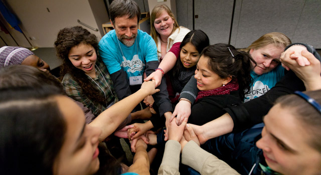 A small group of students, staff and faculty join hands at the Explore!