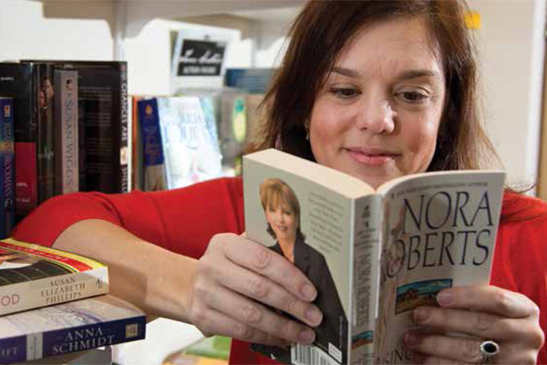 Professor of Sociology Joanna Gregson reads a novel by Nora Roberts, one of the highest-selling romance authors of all time. Gregson interviewed Roberts as part of her research on the writers of romance novels.