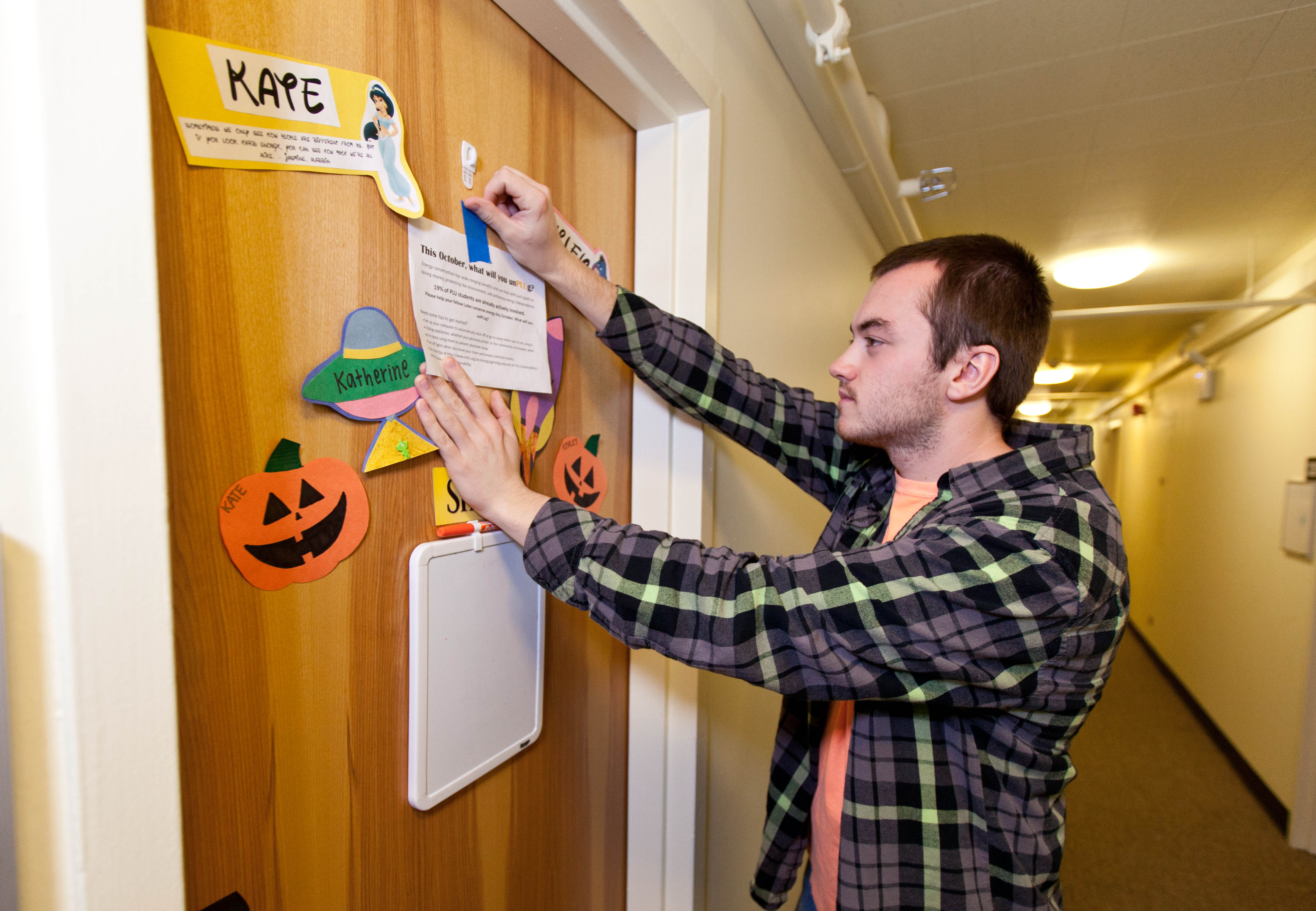 Neil Wagner posts a flyer on the door of a residence-hall room. (Photo: John Froschauer/PLU)