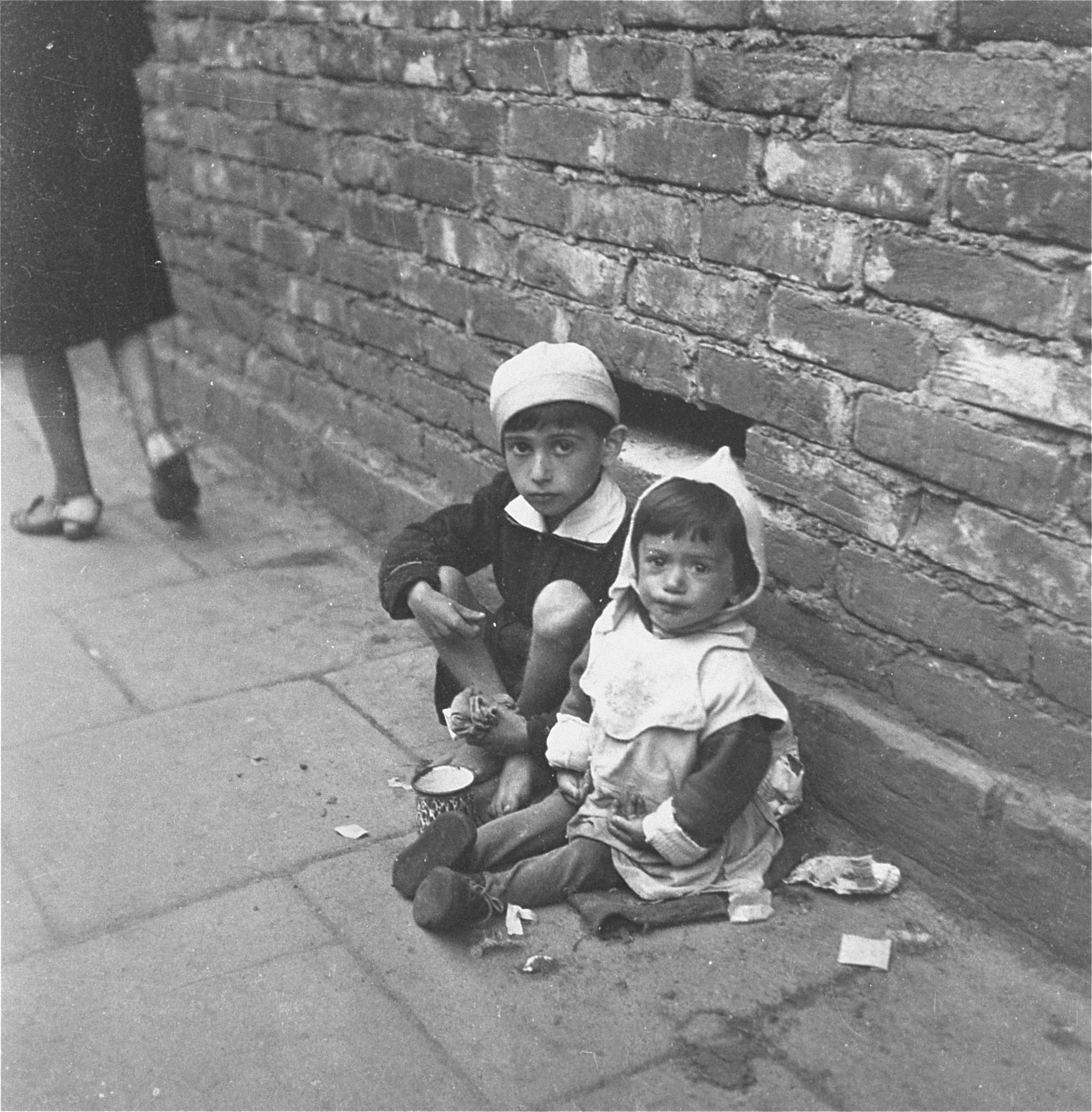 Two young children sitting on the sidewalk eating