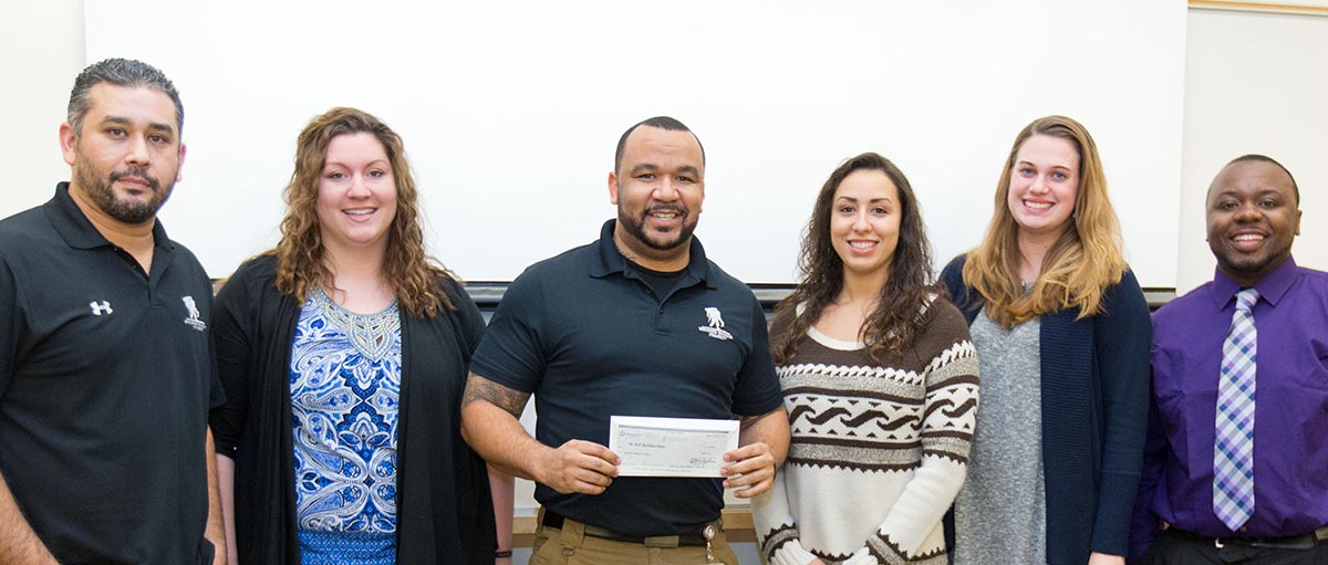 PLU business students Bree Watkins '16, Liandra Daniels '16, Jillian Stanphill ‘16 and Freddie Fisher ‘16 present Gary Cashman and Nino Gray Jr. of the Wounded Warrior Project a $500 donation. (Photo by John Froschauer/PLU)