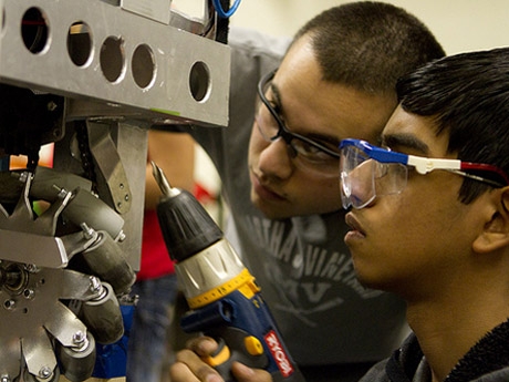 Two students with safety glasses drilling into a metal object