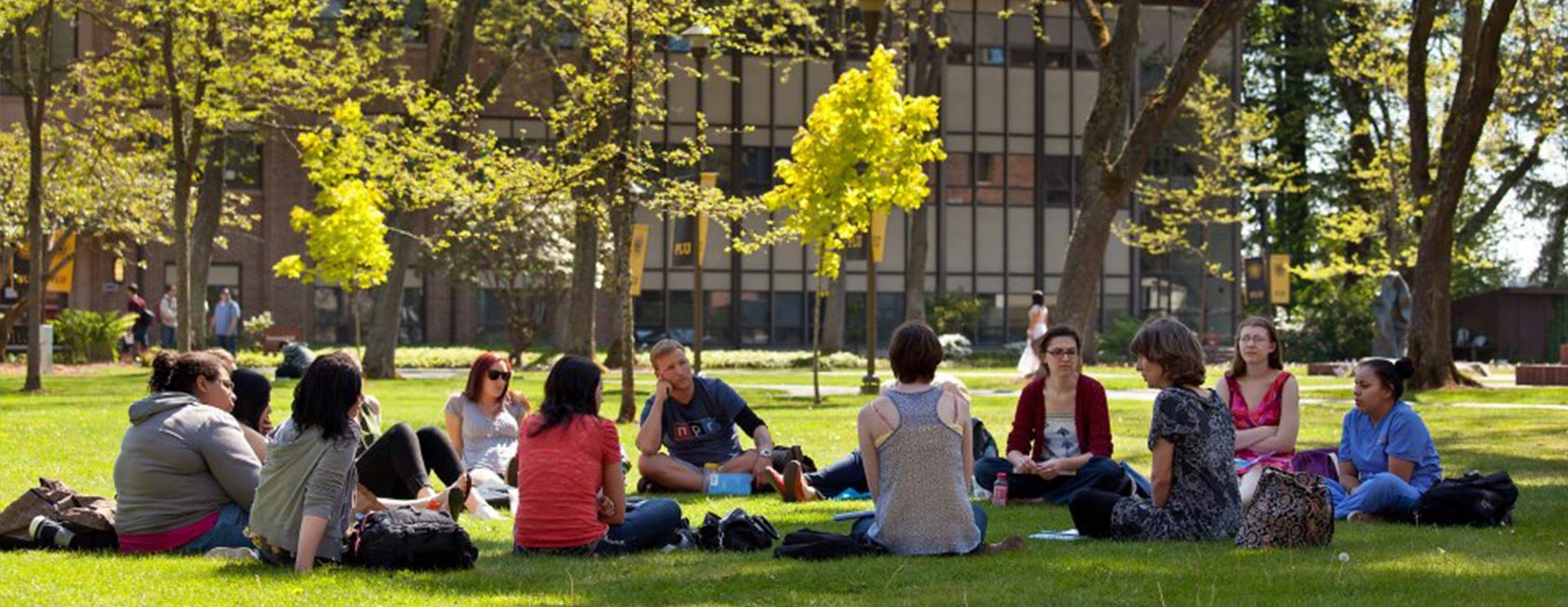 A PLU class sits in a circle on a campus lawn on PLU's upper campus