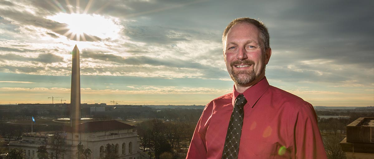 Scott Foss '91 on the rooftop of the Department of the Interior building with the Washington Monument behind him.