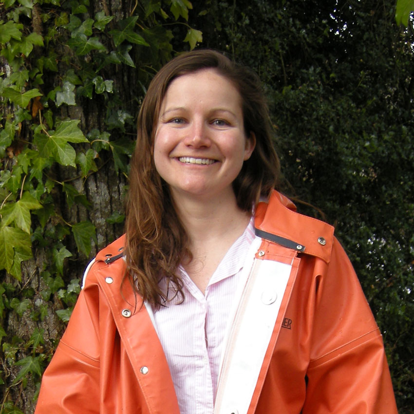 PLU professor Claire Todd smiles while standing in front of a large tree trunk near Clover Creek.