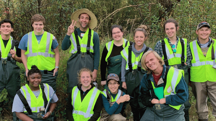 PLU students pose for a photo at Clover Creek, all wearing yellow construction vests over raingear.