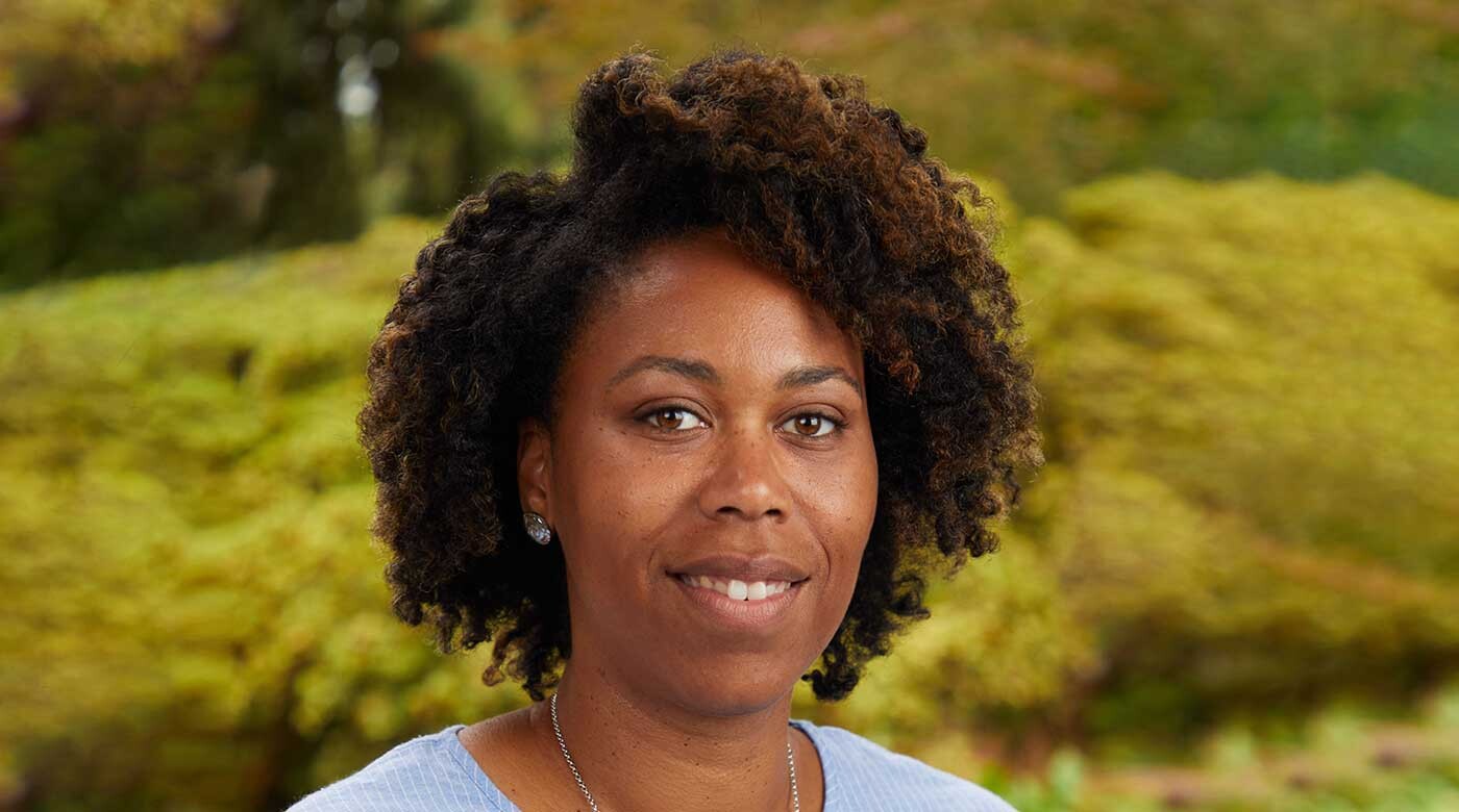 PLU biology professor Lathiena Nervo on campus in front of some bushes.