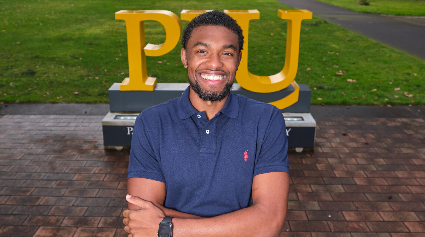 Andre Jones poses in front of PLU sign on campus.