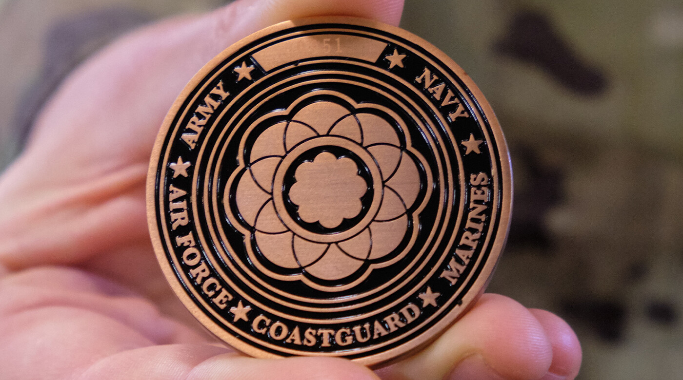 Image of hand holding a coin with PLU's Rose Window engraved and highlighting the branches of the US Military.