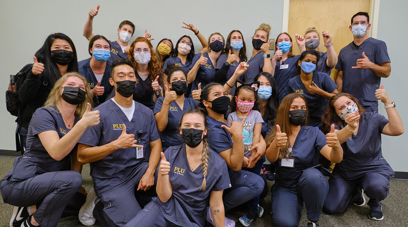 Nursing students in their nursing scrubs giving a thumbs up to the camera at the white coat ceremony.