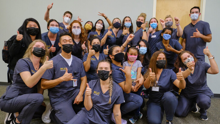 Nursing students in their nursing scrubs giving a thumbs up to the camera at the white coat ceremony.