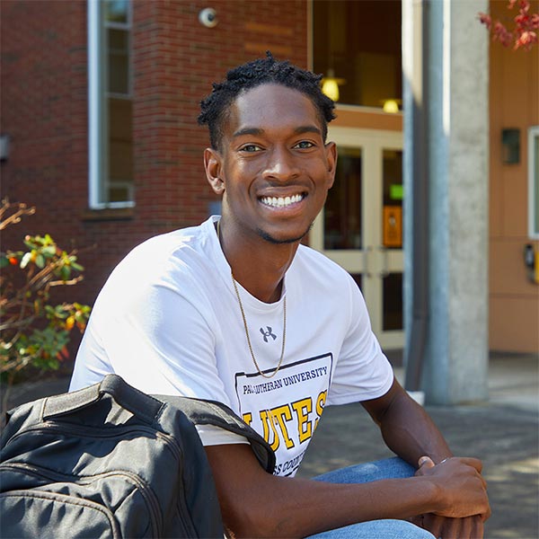 RHA president Hezekiah Goodwin ’22 sits, smiling outside south hall holding his packpack on a sunny fall day