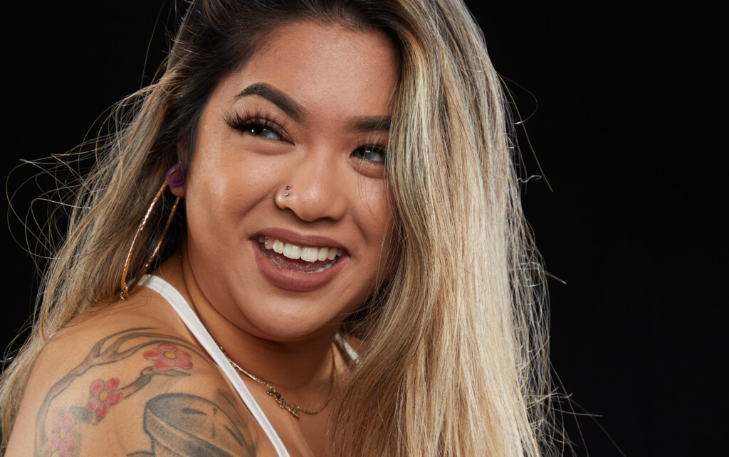 April Reyes smiles into the camera, a close up of her face in front of black background.