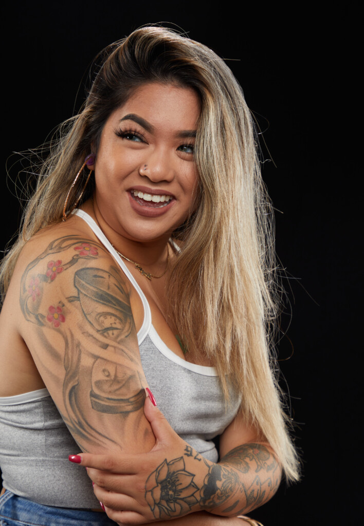 April Reyes smiles into the camera while showing off a colorful tattoo on her right shoulder.
