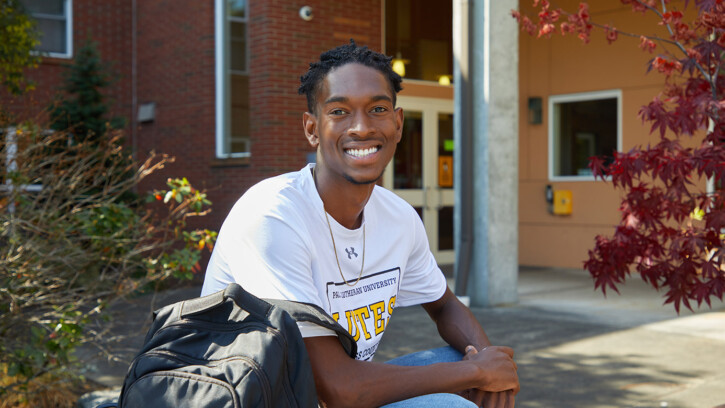 RHA president Hezekiah Goodwin ’22 sits, smiling outside south hall holding his packpack on a sunny fall day