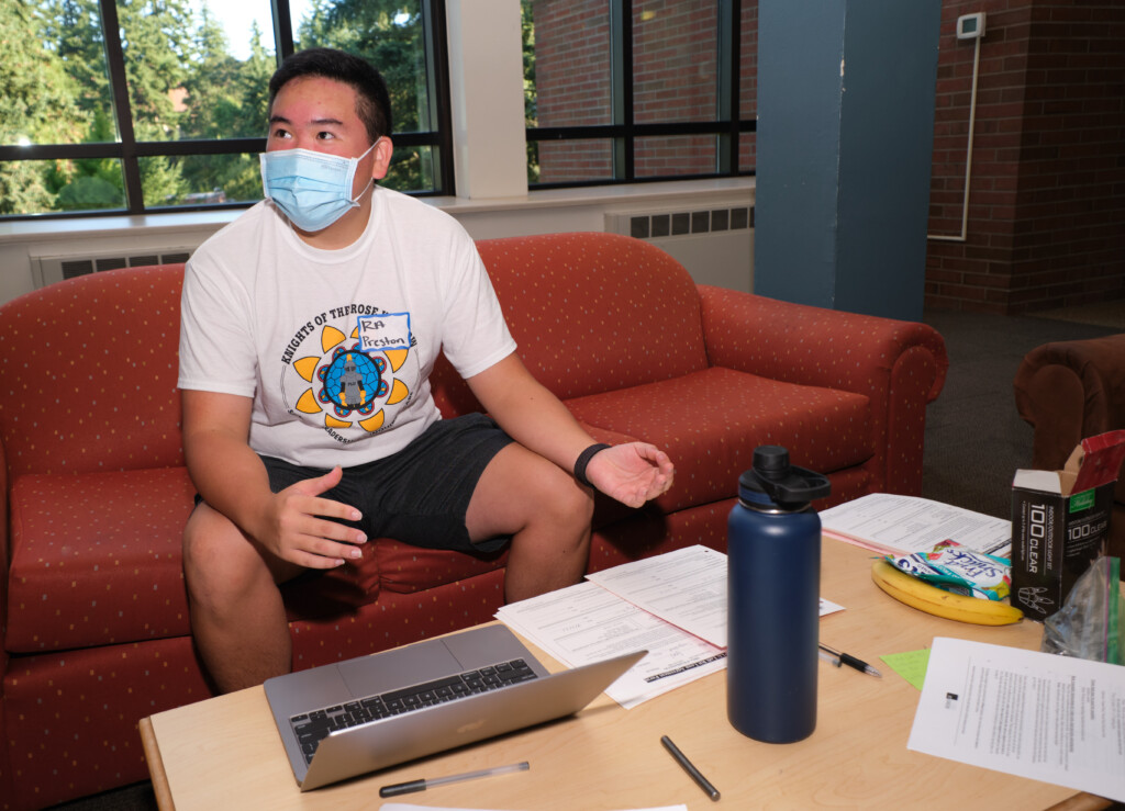 Preston Gee ’24 talking while sitting on a red coach, wearing a blue mask.