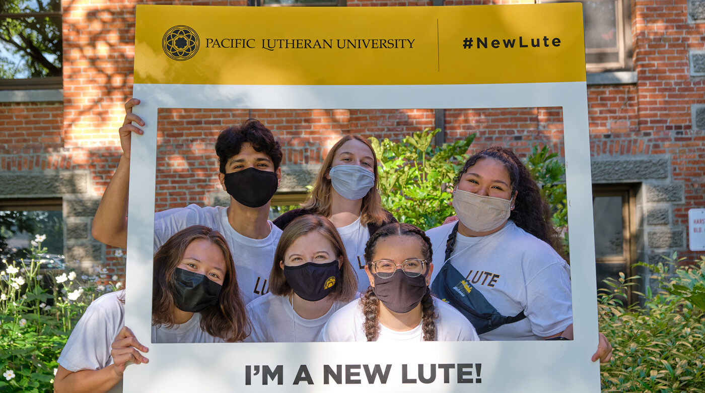 six PLU students wearing protective masks pose with a sign that says "I'm a New Lute"