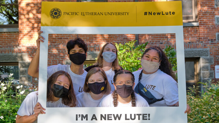 six PLU students wearing protective masks pose with a sign that says "I'm a New Lute"