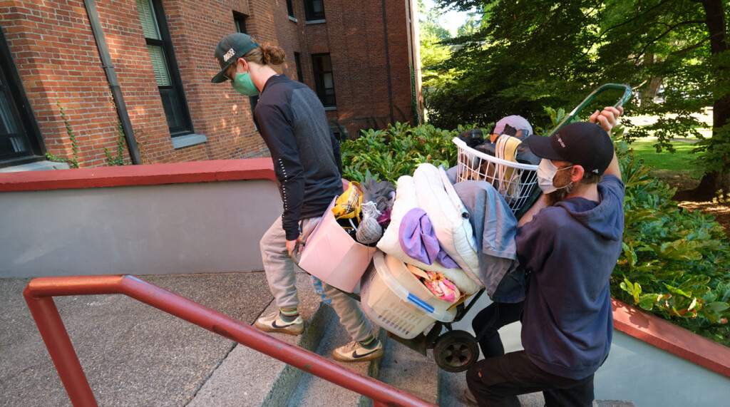 Two masked lutes work together to carry a cart of bags and belongs up a staircase outside Harstad Hall during move in.