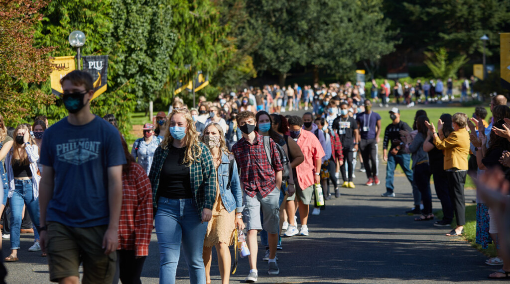 a wide photo of more than 100 students walking on the path next to Foss Field, on their way to convocation.