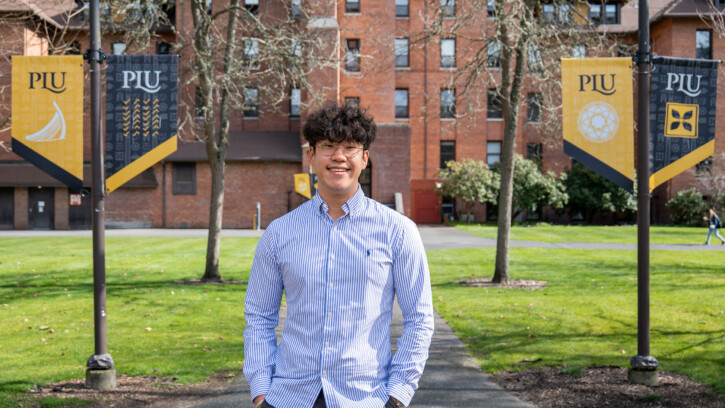 David Yun smiles at the camera while standing on upper campus in front of Harstad Hall.