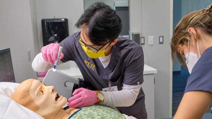 Image of PLU Nursing Student inspecting a mannequin patient that is laying down in a live nursing simulation room
